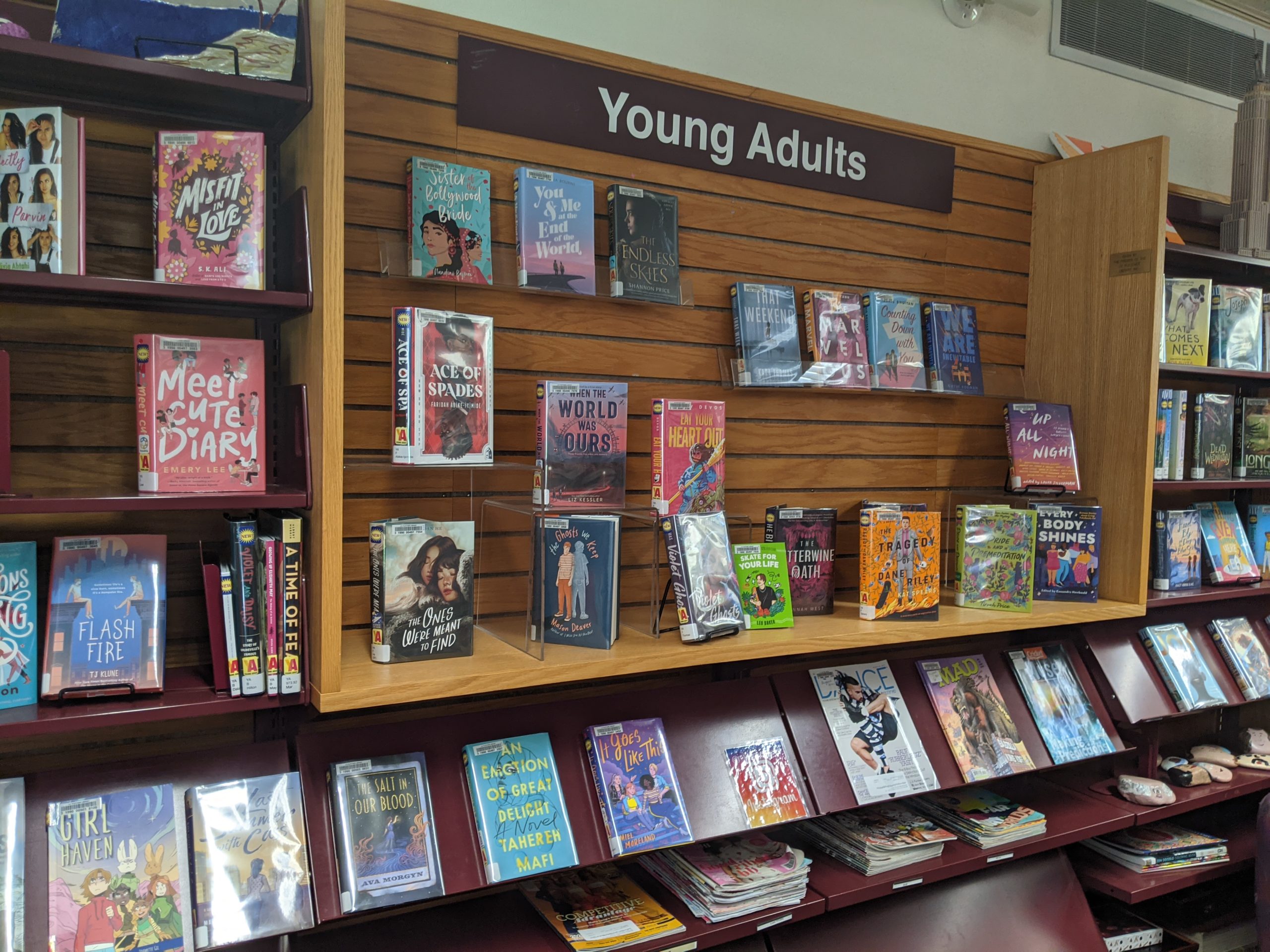 A slatted brown wall with floating shelves filled with colorful new young adult books.